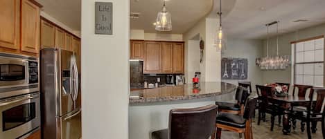 A modern kitchen with stainless steel appliances, a central island with bar stools, and a sign stating "Life Is Good".