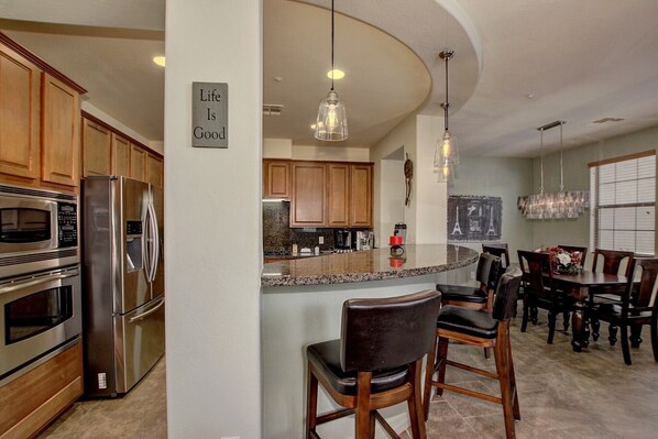 Una cocina moderna con electrodomésticos de acero inoxidable, una isla central con taburetes y un cartel que dice "Life Is Good".