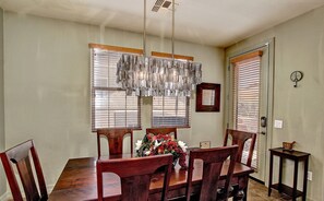 Un comedor con una mesa y sillas de madera, una araña y un jarrón con flores.