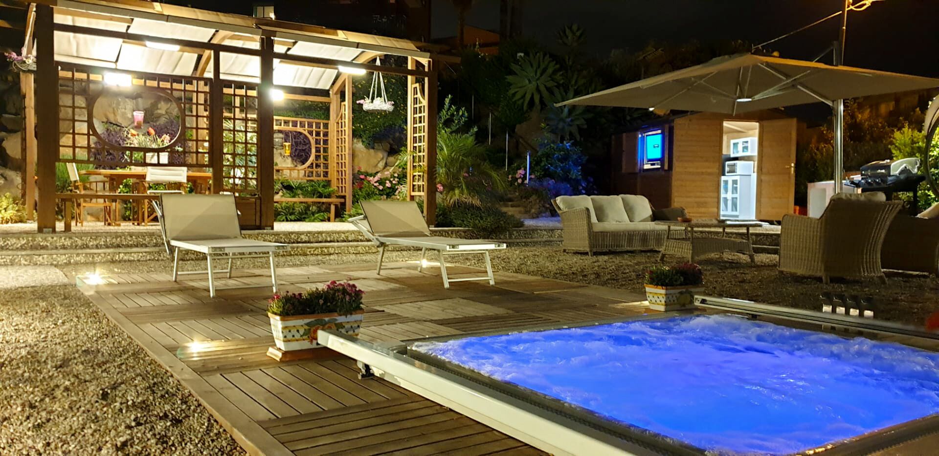 A well-lit outdoor area with a hot tub, lounge chairs, and a wooden pergola.