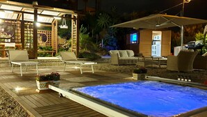 A well-lit outdoor area with a hot tub, lounge chairs, and a wooden pergola. - Cyclope's House.  Amazing view and private mini SPA. (Vampolieri I)