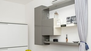 A modern, compact room with a white desk, black chairs, a flat-screen TV, a mounted air conditioner, and a grey curtain. - FIUMICINO BUSINESS & VACATION APARTMENT CIR 5572 (Fiumicino)