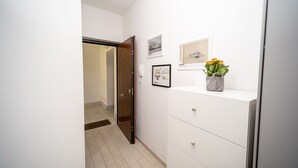 A hallway with a white wall, a wooden door, and a white cabinet with a vase of flowers. - FIUMICINO BUSINESS & VACATION APARTMENT CIR 5572 (Fiumicino)