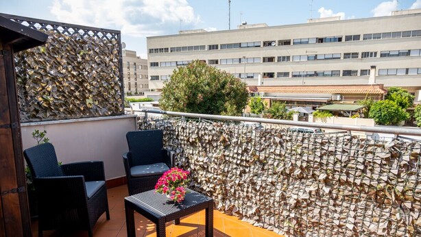 A balcony with wicker furniture, a small table with flowers, and a decorative wall. - FIUMICINO BUSINESS & VACATION APARTMENT CIR 5572 (Fiumicino)