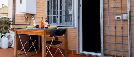 A patio with a table, chairs, a potted plant, and a sliding door.