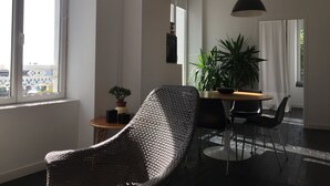 Una sala de estar moderna con un ventanal grande, una silla de mimbre, una mesa de comedor con sillas y una planta en maceta.