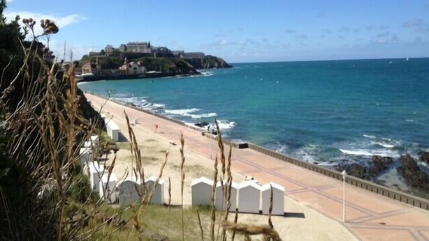 Un paseo marítimo con vistas al mar y un edificio en una colina al fondo.