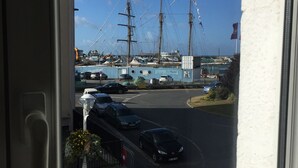 Vista a través de una ventana de un puerto deportivo con veleros, coches estacionados y una farola.