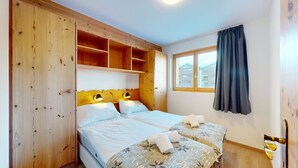 A double bed with a wooden headboard, two bedside tables, a window with curtains, and a view of buildings outside.