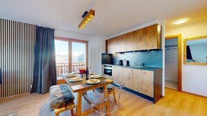 A modern kitchen with wooden cabinets and a blue countertop, a dining area with a wooden table and chairs, and a view of mountains through the window.