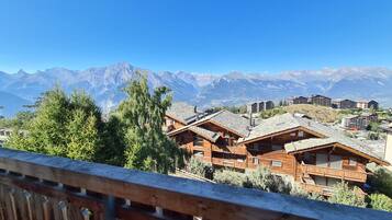 Un rifugio alpino con chalet in legno, una terrazza in legno e vista sulle montagne innevate sullo sfondo.