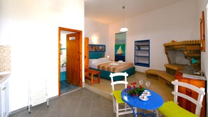 A room with a bed, a dining table with chairs, a sofa, and a small table with a lamp. - JASMINE house. Panoramic pool. Access to the sea. Privileged view of the Egean. (KLIMA)