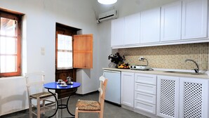 A compact kitchen with white cabinets, a tiled backsplash, a sink, and a small dining table with two chairs. - JASMINE house. Panoramic pool. Access to the sea. Privileged view of the Egean. (KLIMA)