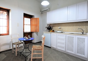 A compact kitchen with white cabinets, a tiled backsplash, a sink, and a small dining area with two chairs.