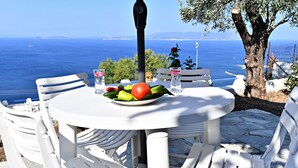 A table with a plate of fruit, white chairs, and a view of the sea. - JASMINE house. Panoramic pool. Access to the sea. Privileged view of the Egean. (KLIMA)