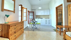 A compact living space with a kitchenette, a dining area with a table and chairs, and a wooden dresser with drawers. - JASMINE house. Panoramic pool. Access to the sea. Privileged view of the Egean. (KLIMA)