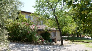 Une maison en pierre avec un toit de tuiles, entourée d’un jardin agrémenté de plantes en fleurs et d’un chemin de gravier.