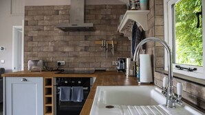 A modern kitchen with a brick backsplash, stainless steel appliances, and a window providing a view of greenery. - Pengelly is Laid back luxury in 9-acres of countryside right near the beach (Kilkhampton, Bude)