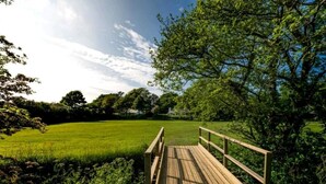 A wooden deck with a railing overlooking a grassy field and trees. - Pengelly is Laid back luxury in 9-acres of countryside right near the beach (Kilkhampton, Bude)
