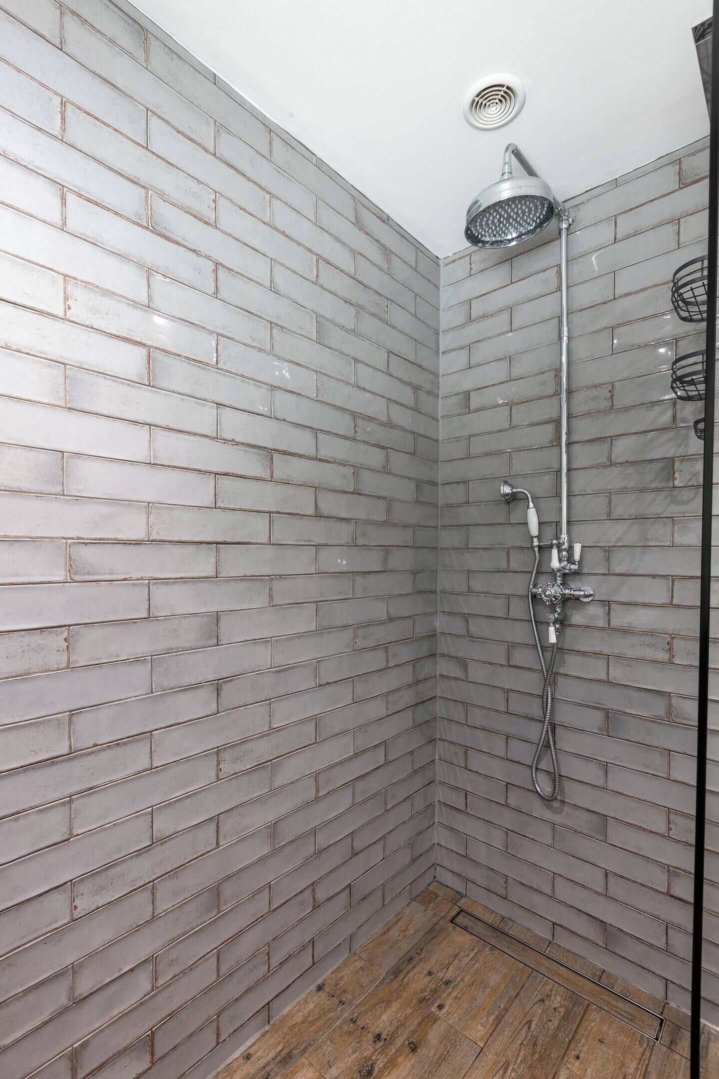 Una ducha de diseño moderno, con pared de ladrillo gris y suelo de madera.