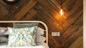 A bedroom with a herringbone wooden ceiling, a bed with a floral pillow, a bedside table, and a hanging light fixture. - Pengelly is Laid back luxury in 9-acres of countryside right near the beach (Kilkhampton, Bude)
