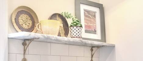 A kitchen with white subway tiles, a green stand mixer, and a shelf with decorative items.
