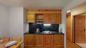 Eine kleine Küche mit Holzschränken, einer Mikrowelle, einer Kaffeemaschine und einem Spülbecken.