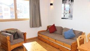 A cozy room with a wooden sofa, a wooden chair, a small wooden table, and a window with a view of buildings outside. - Pracondu 1 306 - OUTDOOR & FUN  charming apartment (Haute-Nendaz)
