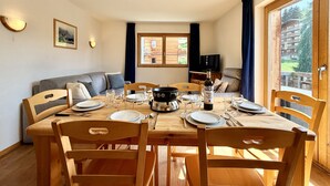 A dining area with a wooden table set for four, surrounded by chairs, with a television and a window in the background. - Pracondu 1 405 - OUTDOOR & FUN  apartment 6 pers (Haute-Nendaz)