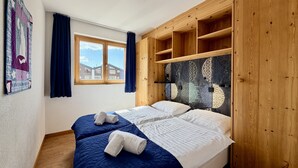A bedroom with two beds, a window with curtains, a quilt on the wall, and a wooden headboard with shelves. - Pracondu 1 405 - OUTDOOR & FUN  apartment 6 pers (Haute-Nendaz)