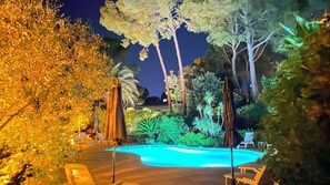 A nighttime view of a swimming pool surrounded by palm trees and lounge chairs. - Apartment T4 MISTRAL 100m2, with terrace 25m2, swimming pool, beach nearby (Saint-Raphaël)