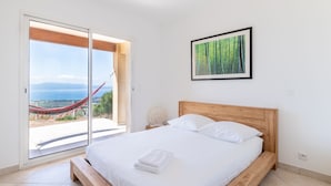 Un dormitorio con una cama grande, una hamaca fuera de la puerta corrediza, un cuadro en la pared y vista al mar.