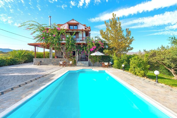 A two-story house with a swimming pool, outdoor furniture, and a garden.
