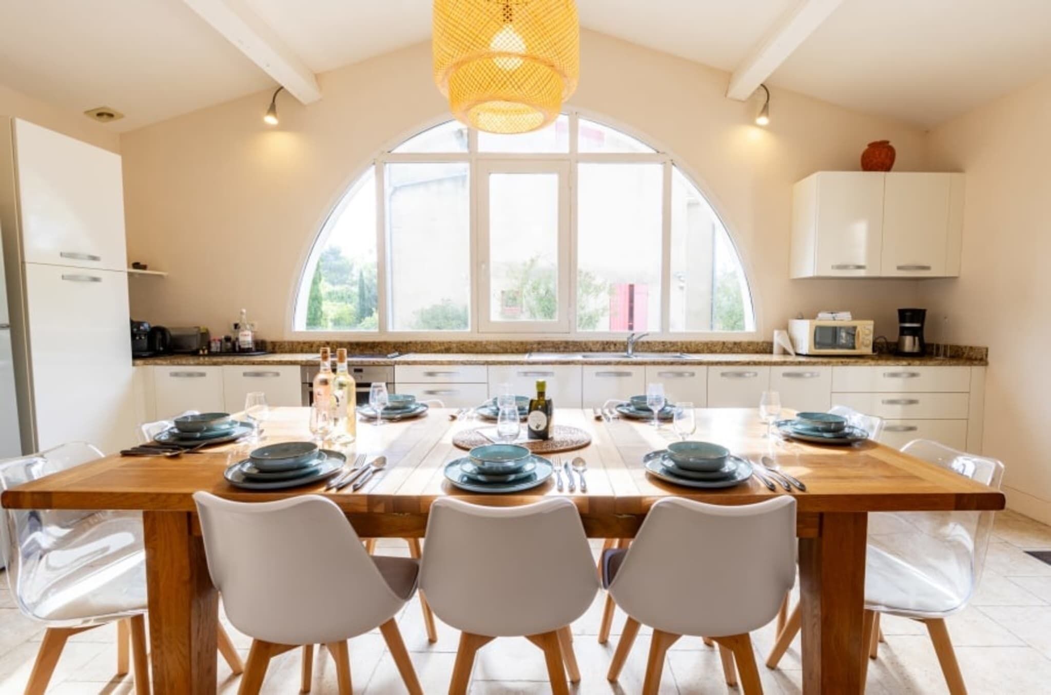 Een moderne keuken met een groot eiland, witte kasten en een groot raam dat zorgt voor veel daglicht.