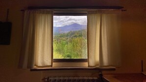 Een kamer met een raam dat uitkijkt op een bergachtig landschap.