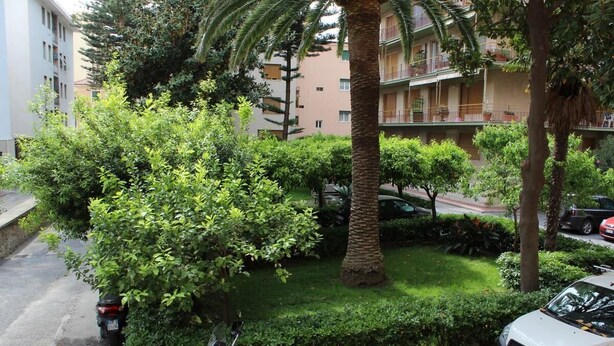 A residential area with a well-maintained lawn, a parked motorcycle, and a car. There are multi-story buildings in the background. - Miramare 2 appartamento trilocale in complesso residenziale (TAGGIA)
