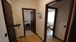 A hallway with a carpeted floor, a radiator, and a door leading to a room with a bed and a window. - Miramare 2 appartamento trilocale in complesso residenziale (TAGGIA)