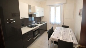 A compact kitchen with dark cabinets, a white countertop, and a dining table with a tablecloth. - Miramare 2 appartamento trilocale in complesso residenziale (TAGGIA)
