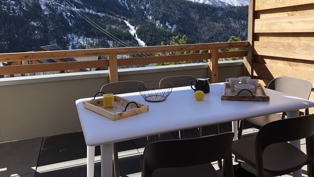 Une table dressée à l’extérieur, avec une vue sur les montagnes, une balustrade en bois et un ciel dégagé.