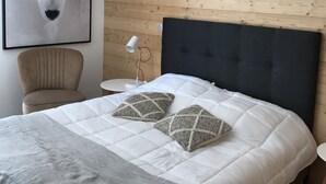 Une chambre moderne avec un grand lit, une tête de lit en bois, un luminaire suspendu blanc, une œuvre d’art représentant un ours polaire encadrée, une table ronde et une chaise.