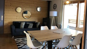 Un salon moderne avec un mur en bois, un canapé foncé, une table à manger en bois avec des chaises et un grand miroir.