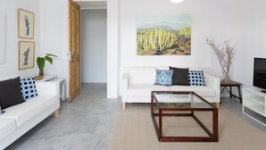 A modern living room with a white sofa, a glass coffee table, and a cactus painting on the wall. - VILLA EL MATO - CASERÍO DE GUAZA (Arona)