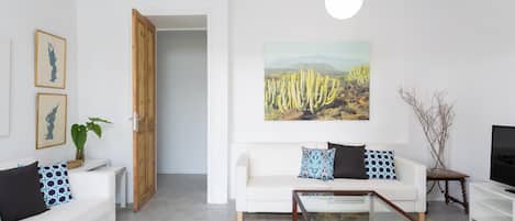 A modern living room with a white sofa, a glass coffee table, and a cactus painting on the wall.