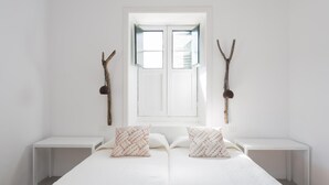 A minimalist bedroom with a large bed, two bedside tables, a window with open shutters, and two wall-mounted branches. - VILLA EL MATO - CASERÍO DE GUAZA (Arona)