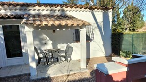 Un espace extérieur aménagé avec une table et des chaises, un coin salon abrité et un bâtiment blanc doté d’un toit en tuiles.