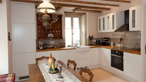 A kitchen with wooden beams, white cabinets, a dining table with a tablecloth, and a hanging light fixture. - Chez Hall, La Grange, 2bdr/2bth converted barn bursting with charm, Meursault (Meursault)