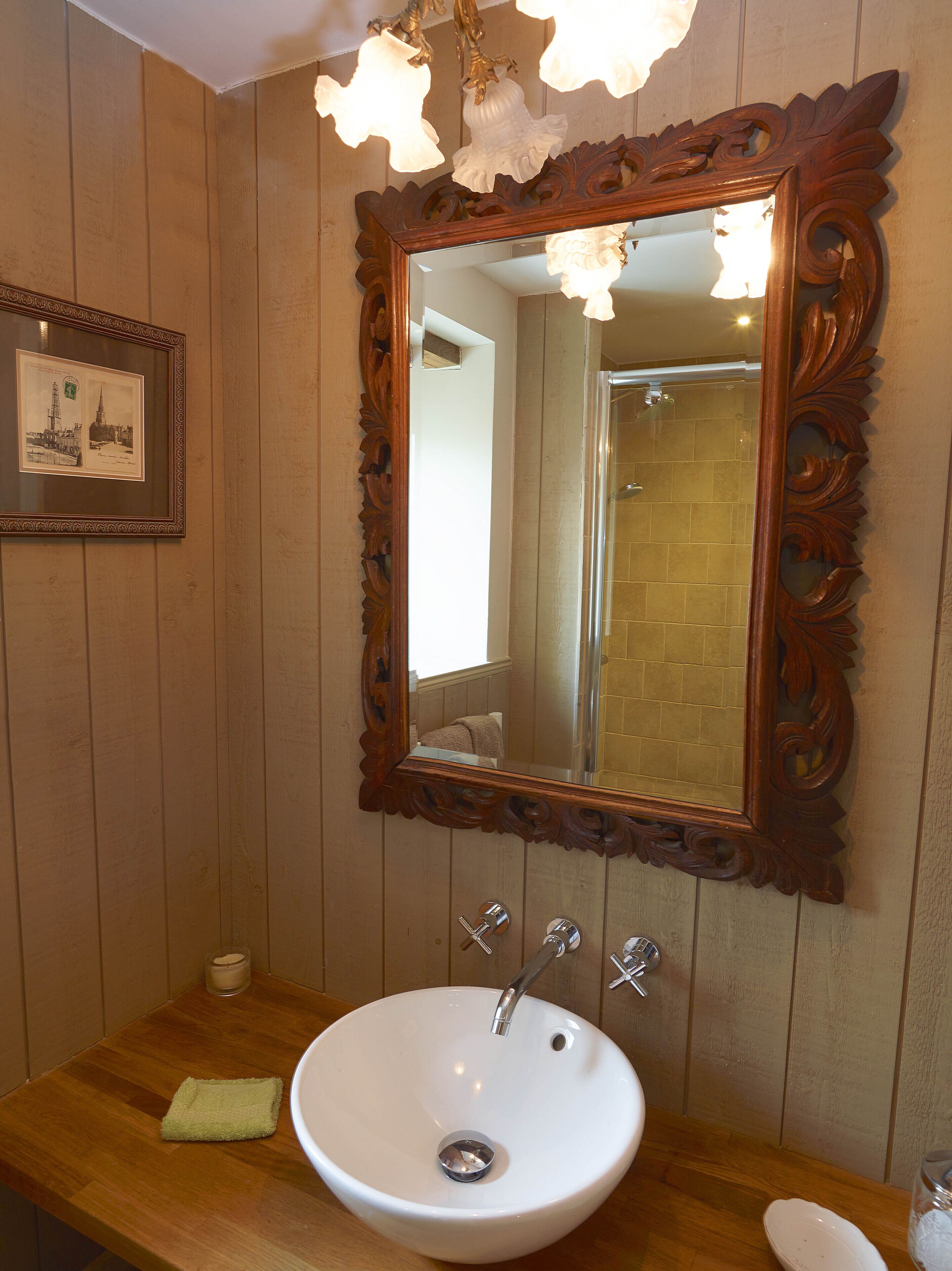 A bathroom with a wooden vanity, a white sink, and a large mirror with an ornate frame.