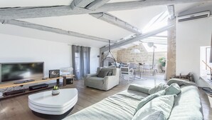 Ein modernes Wohnzimmer mit sichtbaren Holzbalken, einem Flachbildfernseher, einer Couch und einem Essbereich mit Tisch und Stühlen.