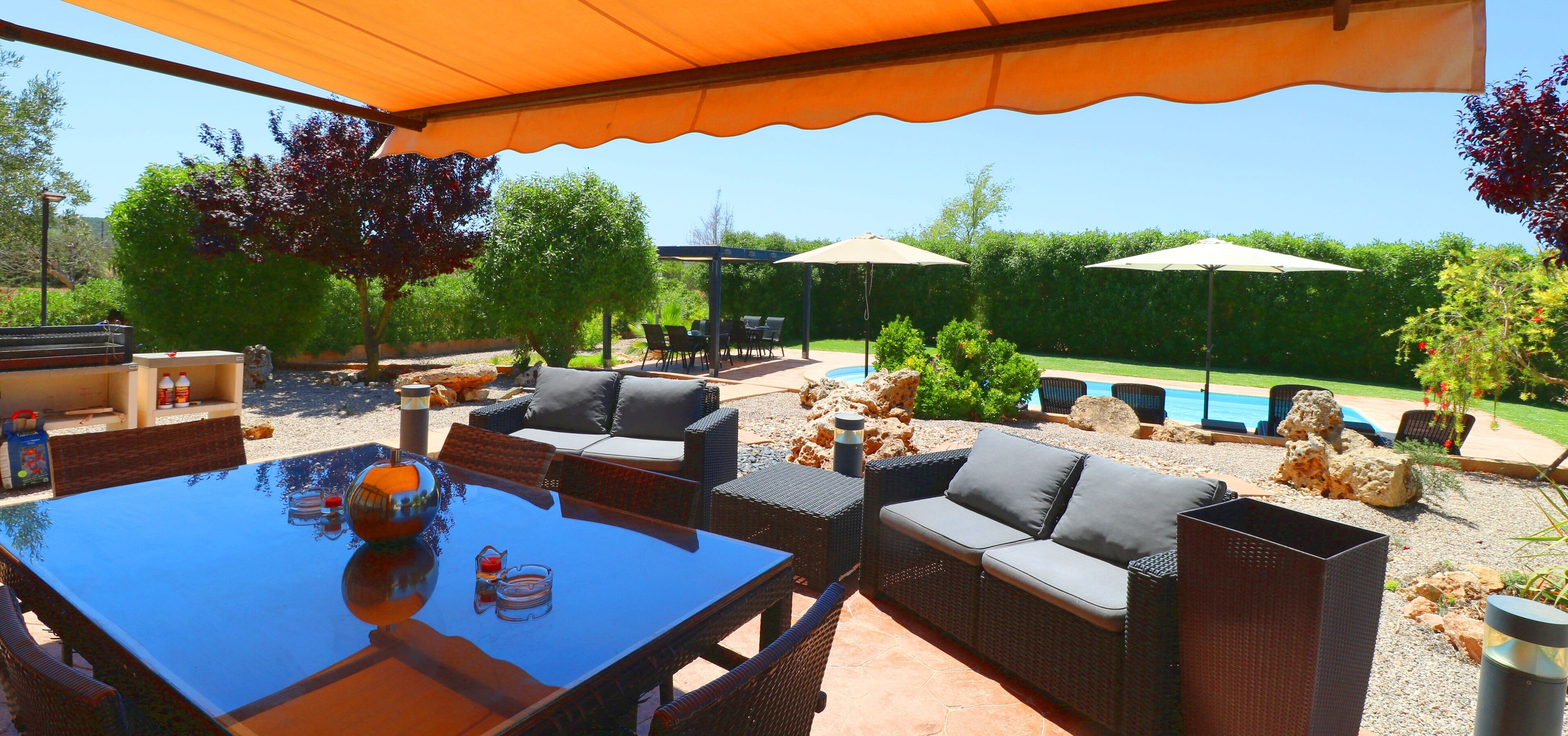 Un espace extérieur aménagé en terrasse, avec une table en verre, des meubles en osier et des parasols pour créer de l’ombre.