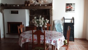 Een eetgedeelte met een ronde tafel, bedekt met een tafelkleed met een patroon, omringd door houten stoelen. Op de tafel staat een vaas met witte bloemen.